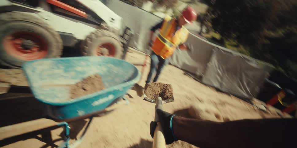 Workers working at a construction site holding a shovel and removing soil and putting it into a blue bucket