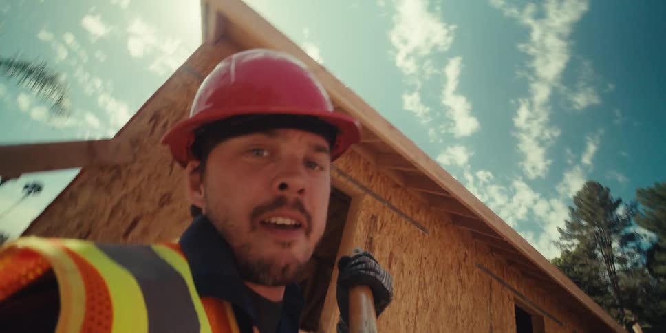The man in the orange hard hat and yellow and orange vest is digging with a shovel