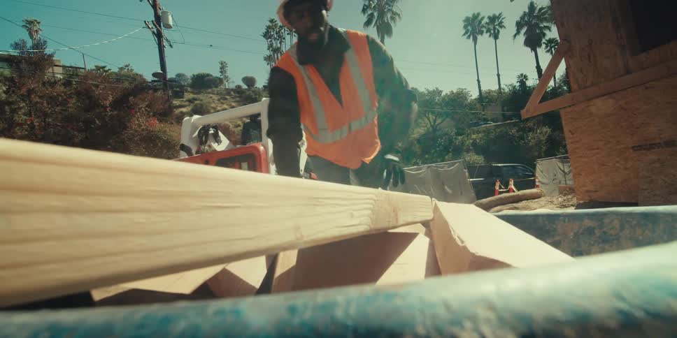 Worker wearing a protective vest and helmet carrying a construction cart with pieces of wood