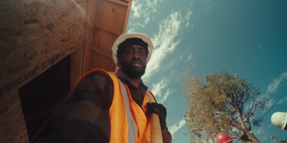 A worker wearing a hardhat and a vest using a shovel at a construction site