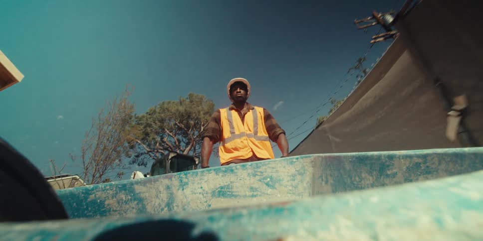 A construction worker wearing a vest and a hardhat pushing a wheelbarrow
