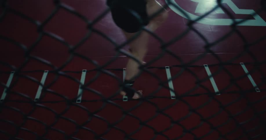 A person performs agility ladder drills in a dimly lit gym