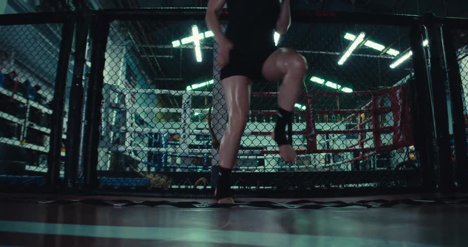 The woman is doing high knees going to the right and she is wearing all black shirts and shirt and she is inside of a mma cage