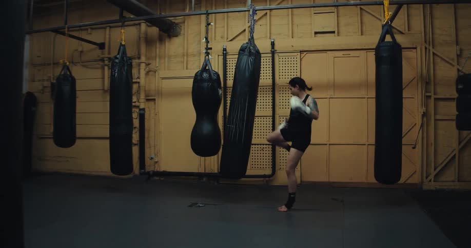 A woman is kicking and punching the heavy bag