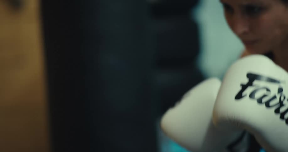 A female boxer is training in a gym by hitting a punching bag