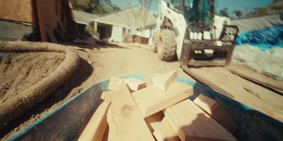 A person pushing a wheelbarrow filled with wooden scraps through a construction site