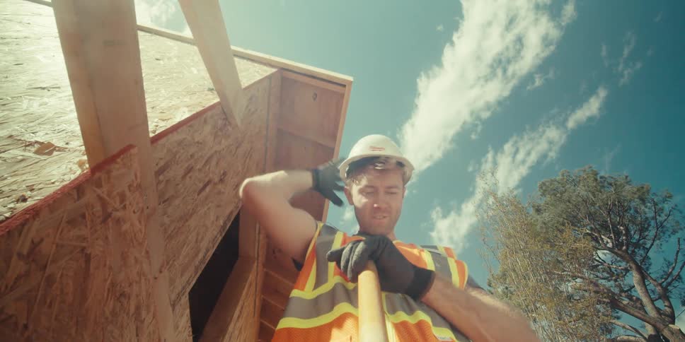 Man on a construction site works on a hot sunny day while two other workers watch him