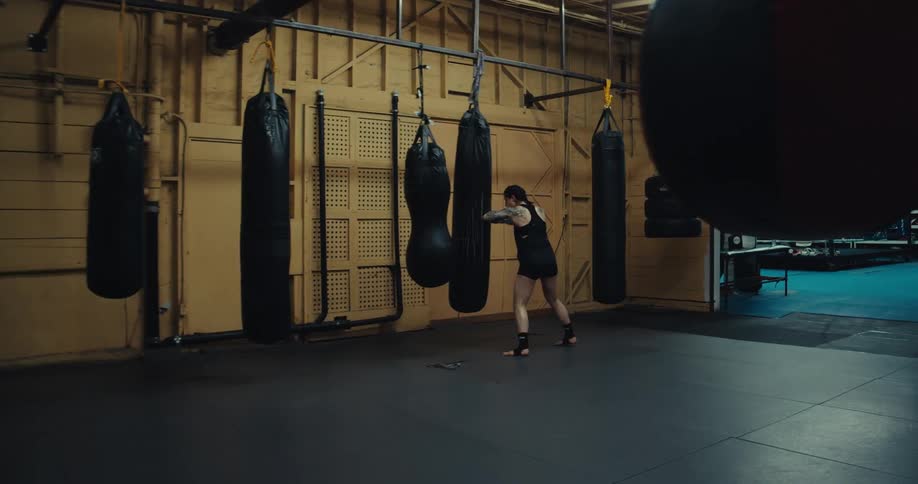 A woman wearing white boxing gloves punches a heavy bag in a spacious gym