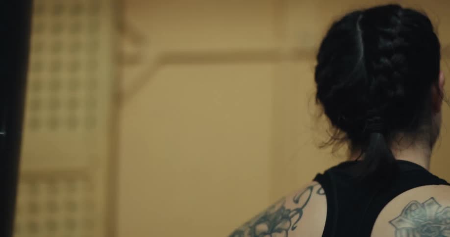 The woman in the black tank top is punching and swinging on a punching bag with her white boxing glove on