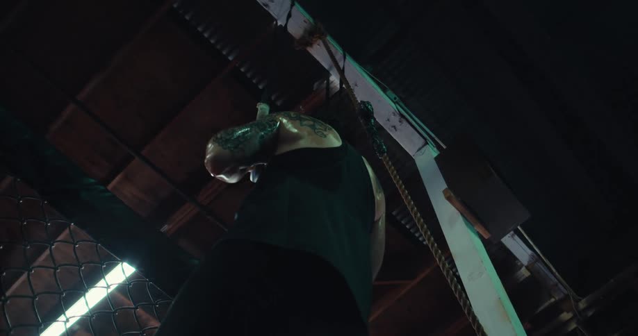 A tattooed individual performs a pullup on gymnastic rings in an indoor gym