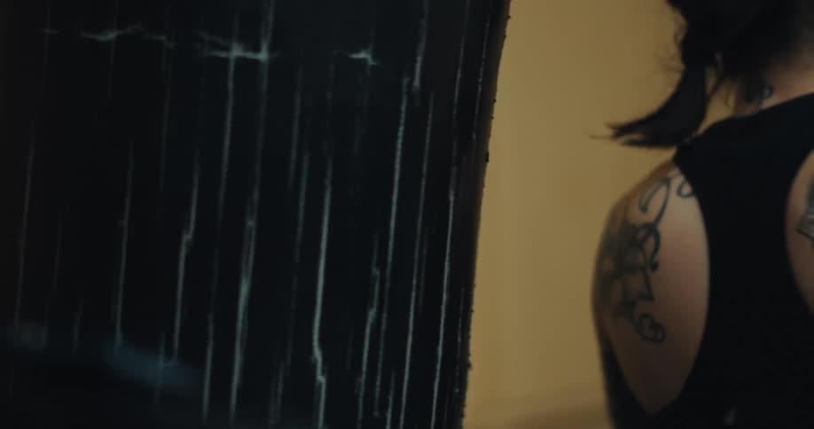 A strong woman with tattooed arms and braided hair practices punching a bag in a gym while wearing white boxing gloves