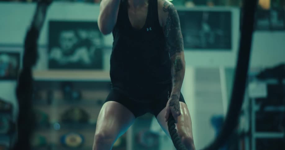 A person in athletic wear is intensely exercising with battle ropes in a gym