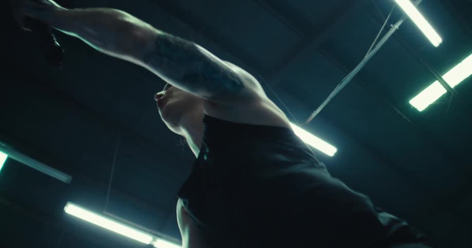 A woman performs battle rope exercises in a gym vigorously moving the ropes in alternating waves