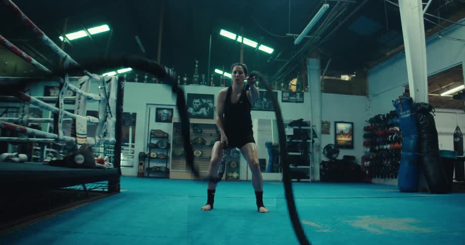 A woman performs battle rope exercises in a gym vigorously moving the ropes in alternating waves