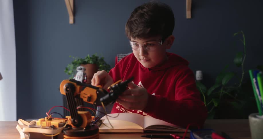 A boy is working on a robot at a table in his house