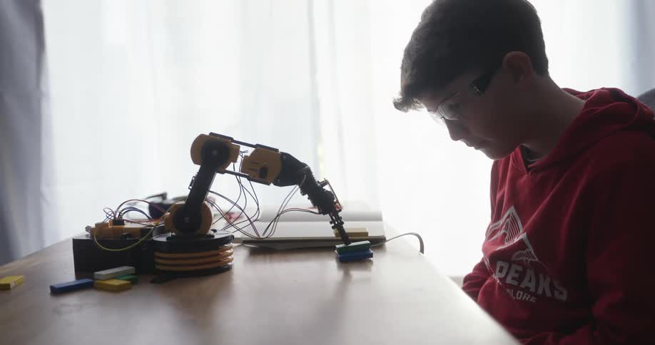 Boy looking intently at a mechanical arm interacting with an object on the table