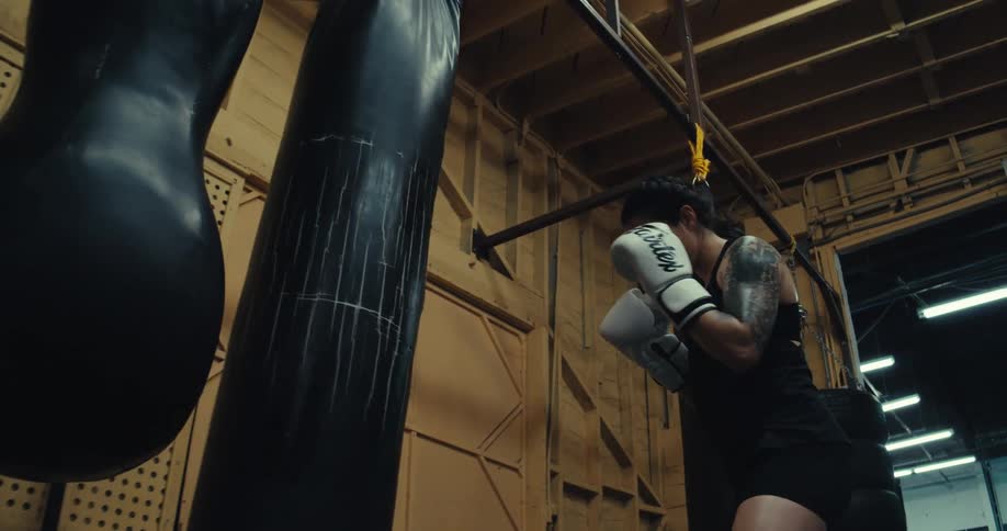 Woman with focused expression delivering high intensity kicks to punching bags