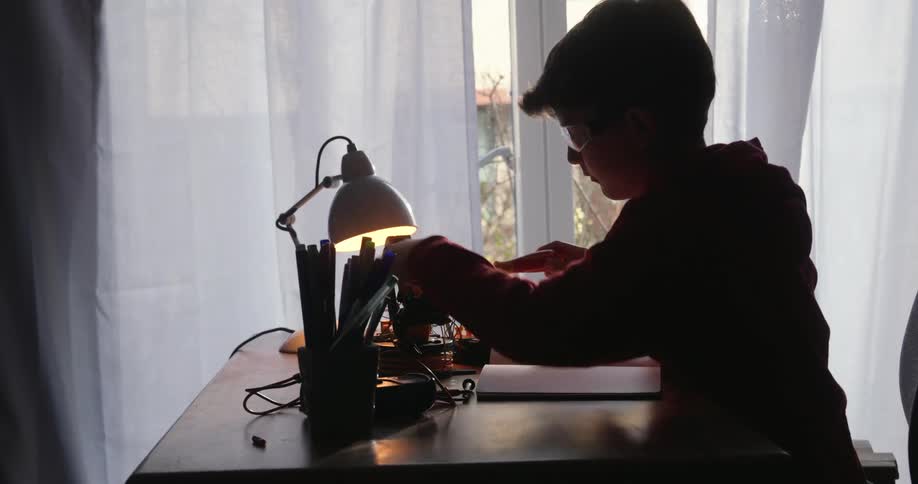 Boy building a small robot sitting in his desk