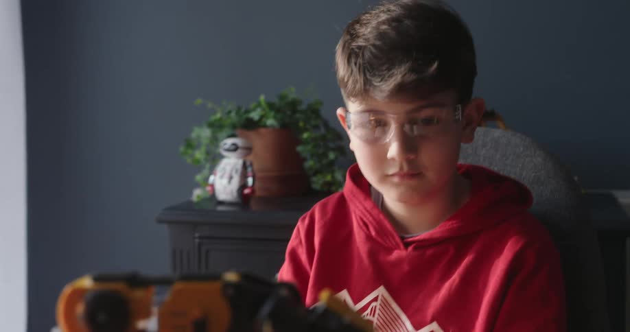 A child in a red hoodie watches as a robotic arm moves in front of an open notebook on a cluttered desk