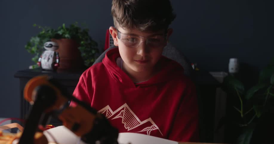 Boy sitting at a table watching a mechanical arm in operation