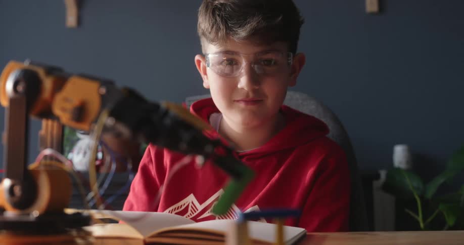 A boy is watching a robotic arm pick up a block