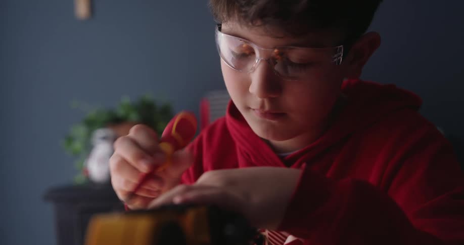 Boy uses a colorful screwdriver on a small machine while in his home
