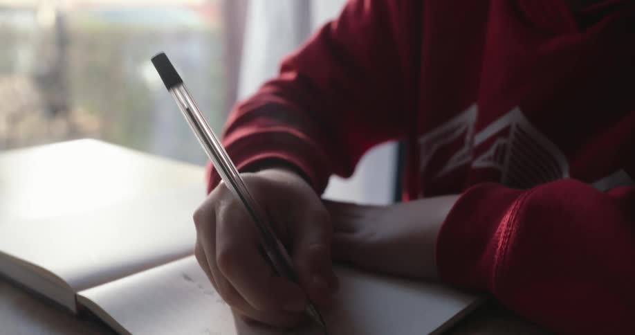 Boy sitting and writing in a notebook with a pen
