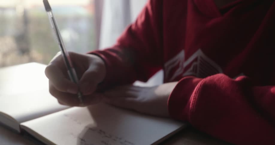 A boys hand writing in a notebook with a pen in hand