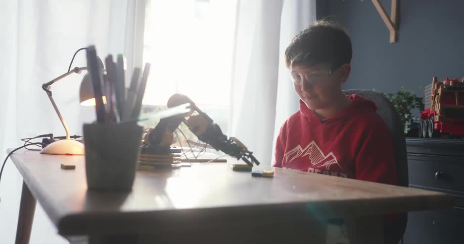 A boy watches his robotic arm try to pick something up