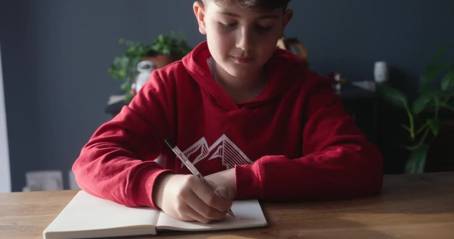 Boy sitting at a table writing in a notebook