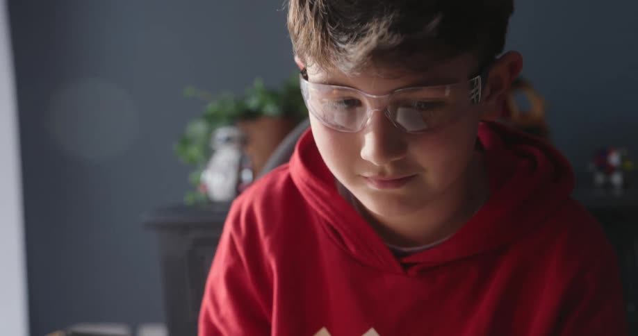 A boy is surveying the robotic arm picking up a block
