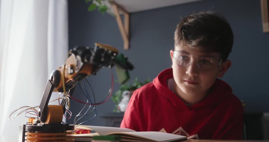 Boy examines the robot arm he has built while sitting at home