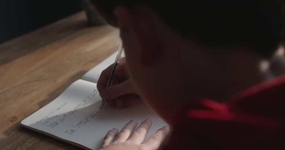 Boy holding a pen and writing in a notebook on the table