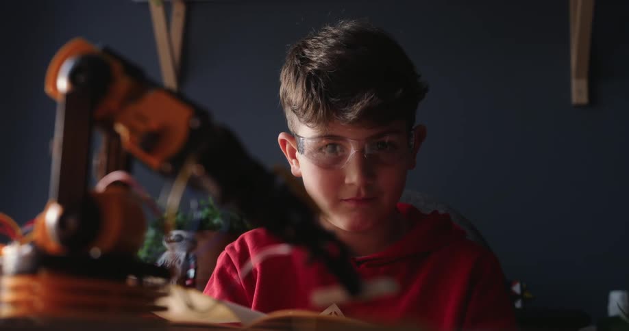 The boy in the red shirt is watching the robotic arm move that he built
