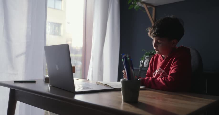 A boy is doing his homework while sitting at a table with a mac book on it