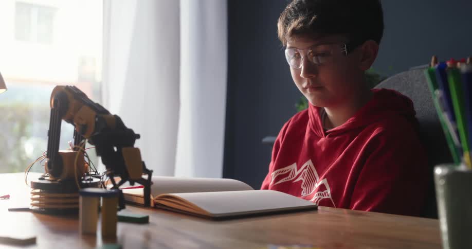 Boy sitting at a table at home watches a robot arm pick up an object