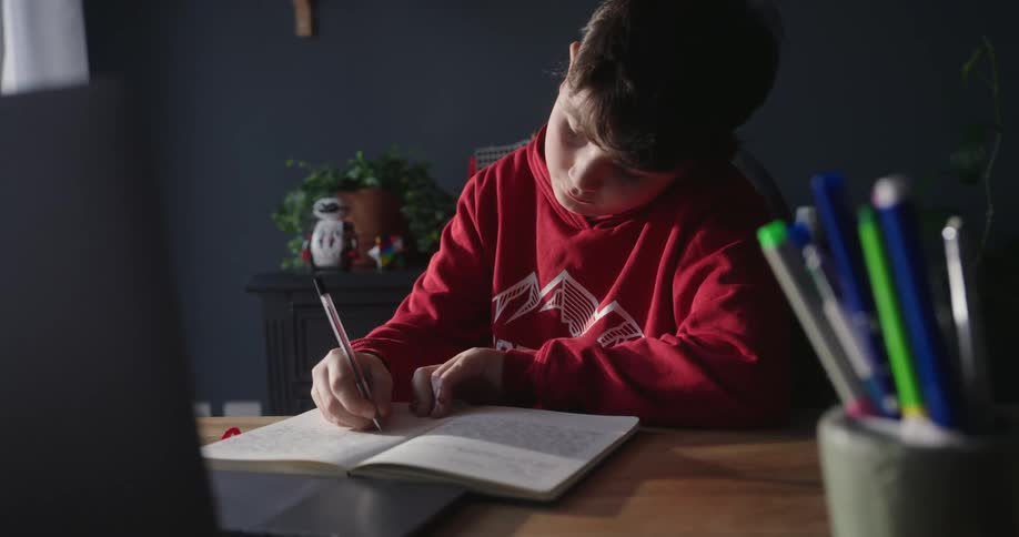 Young boy sitting at his desk in his room writing in a notebook