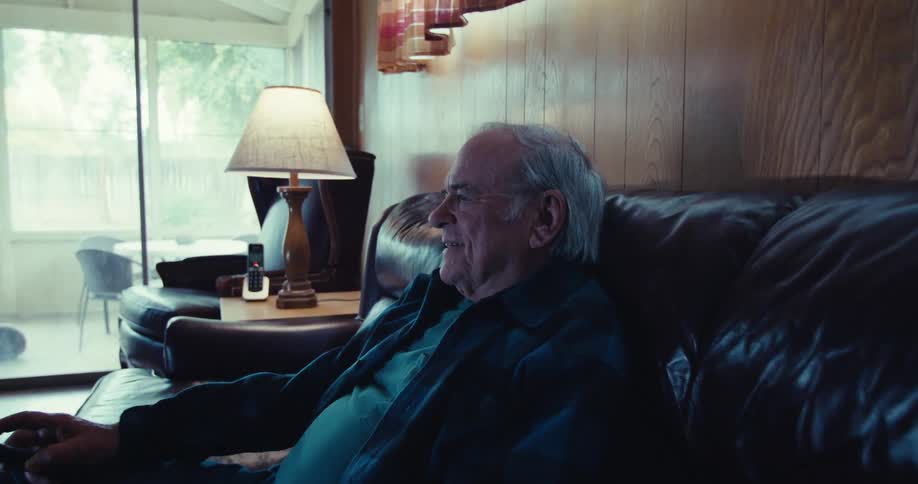 An elderly man smiles and laughs watching television at night
