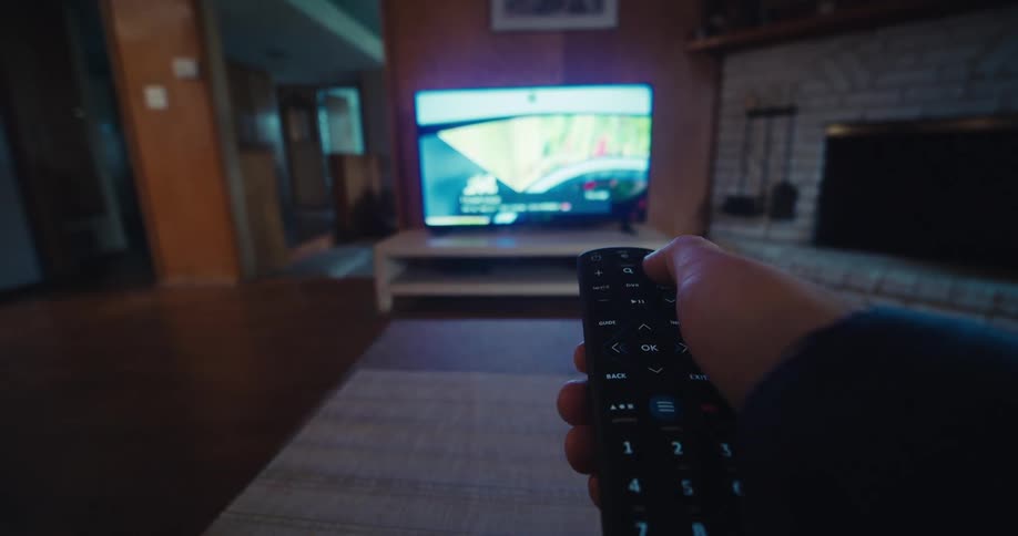 Hand is on the remote control and pointing towards the television