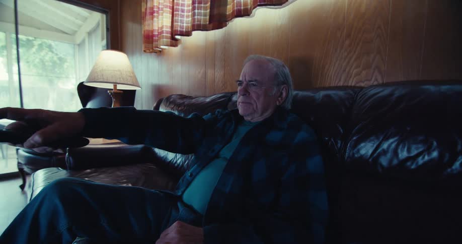 Elderly man smiles and uses his remote while watching television at home alone