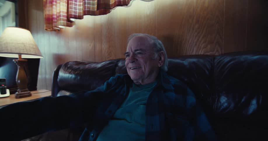 Elderly man sitting on leather sofa in living room and using television remote control