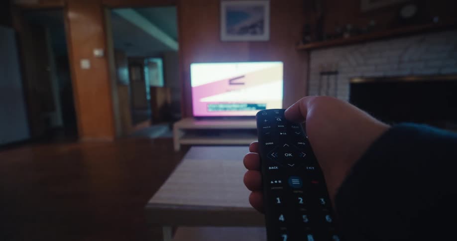A close up of a hand picking up a remote control to change channels on a television