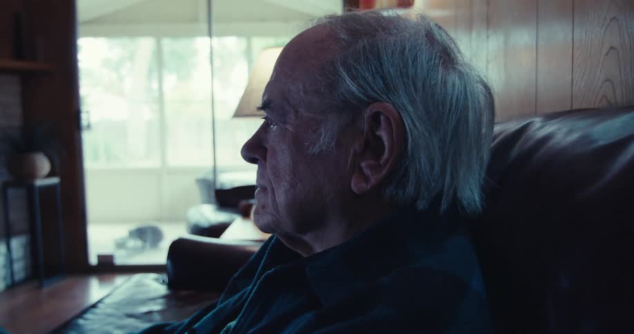 Elderly man sitting in living room on black leather sofa