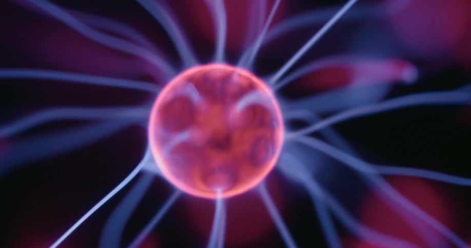 A rotating plasma ball emits swirling arcs of neon light that flow outward from its glowing core each strand flickering in mesmerizing patterns against the dark backdrop creating a dynamic display of luminous energy