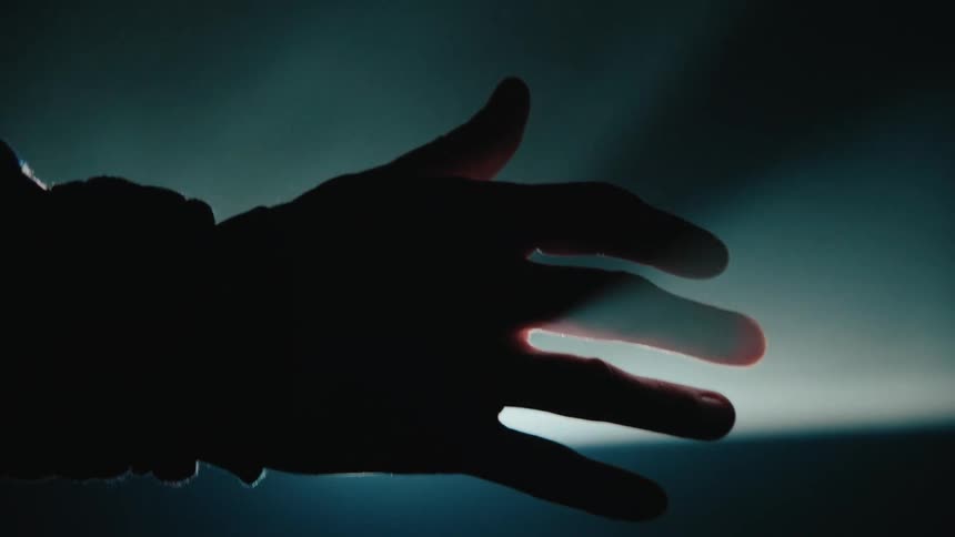 A silhouetted hand reaches into a dimly lit space its fingertips faintly illuminated by a soft glow