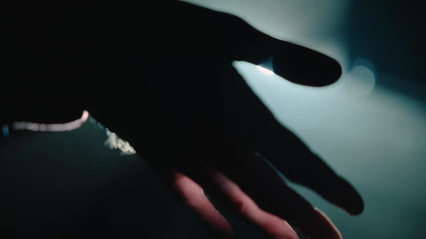 A silhouetted hand reaches into a dimly lit space its fingertips faintly illuminated by a soft glow