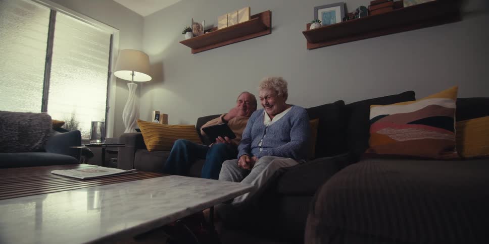 A woman slaps her knees as she laughs at a tablet