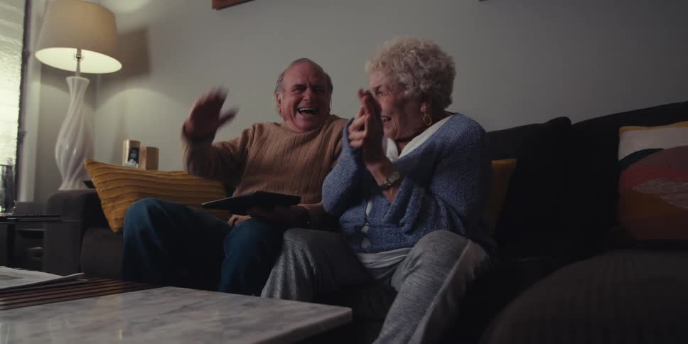 A couple are laughing and having fun watching a tablet