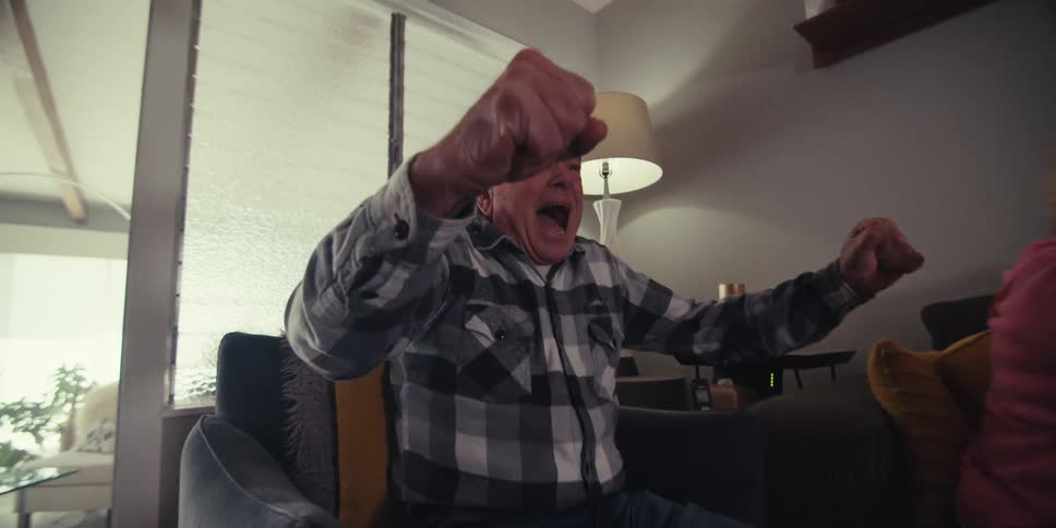 The elderly couple are sitting down cheering on something that can not be seen