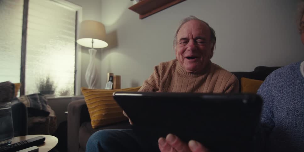 Elderly man and woman interacting with a tablet and laughing